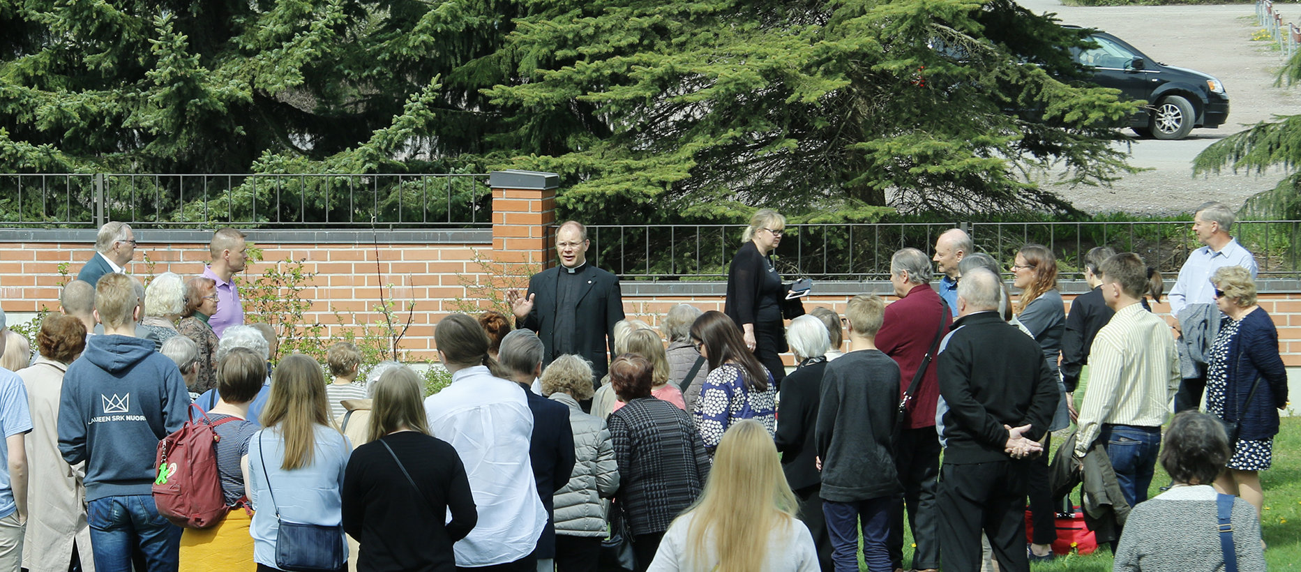 ihmisiä istuttamassa omenapuuta Launeen kirkon pihalla kirkkoherran Heikki Pelkosen johdolla.