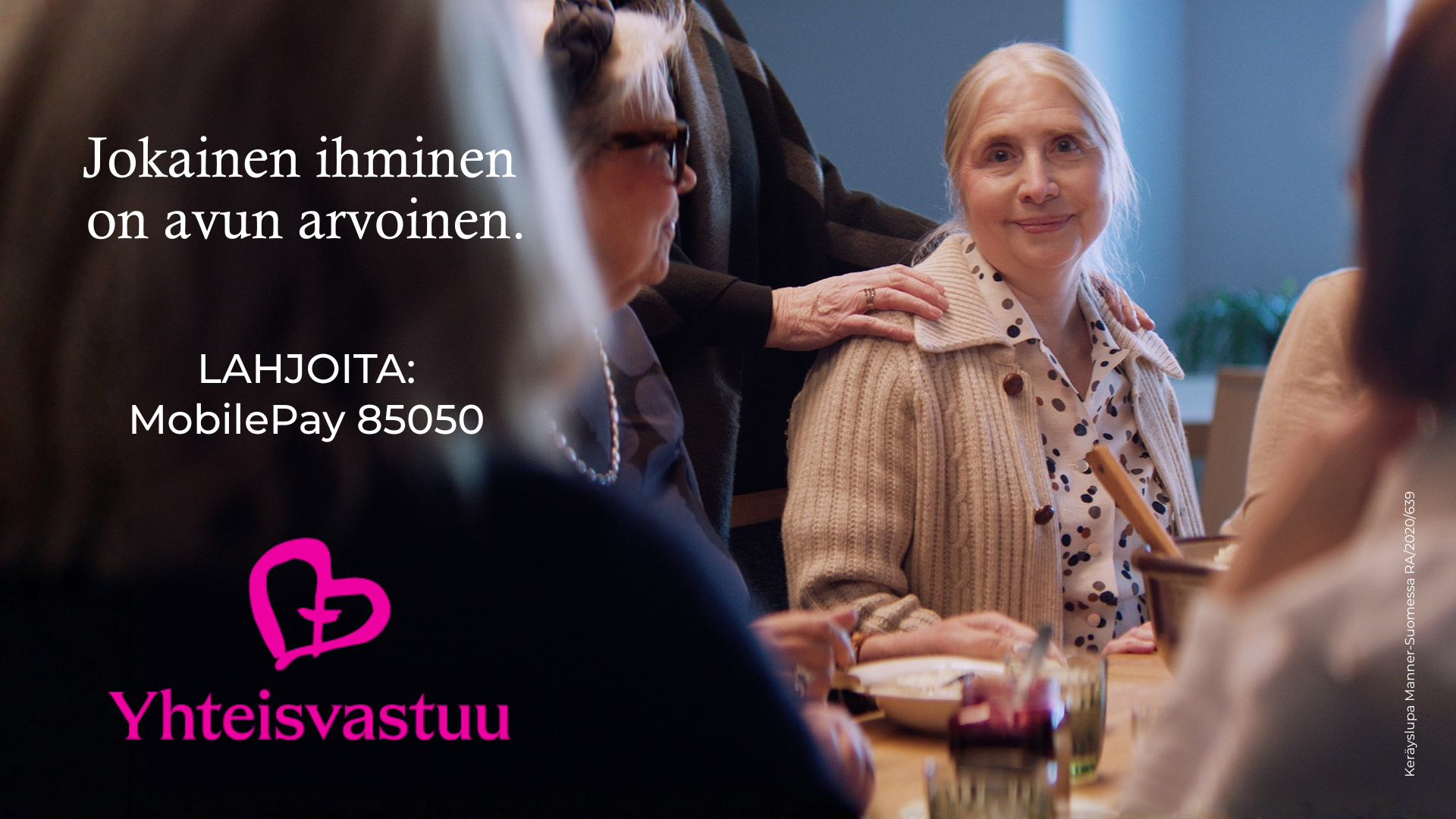 kuvassa on ikääntyvä nainen, joka katsoo kameraan hymyillen. Hänen takanaan on henkilö, joka on painanut kä...