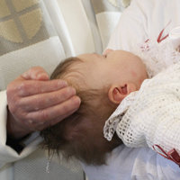 Papin käsi ja vauvan pää kastetilanteessa. 