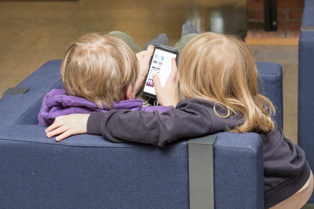Kuvassa on kaksi lasta tutkimassa älypuhelinta.