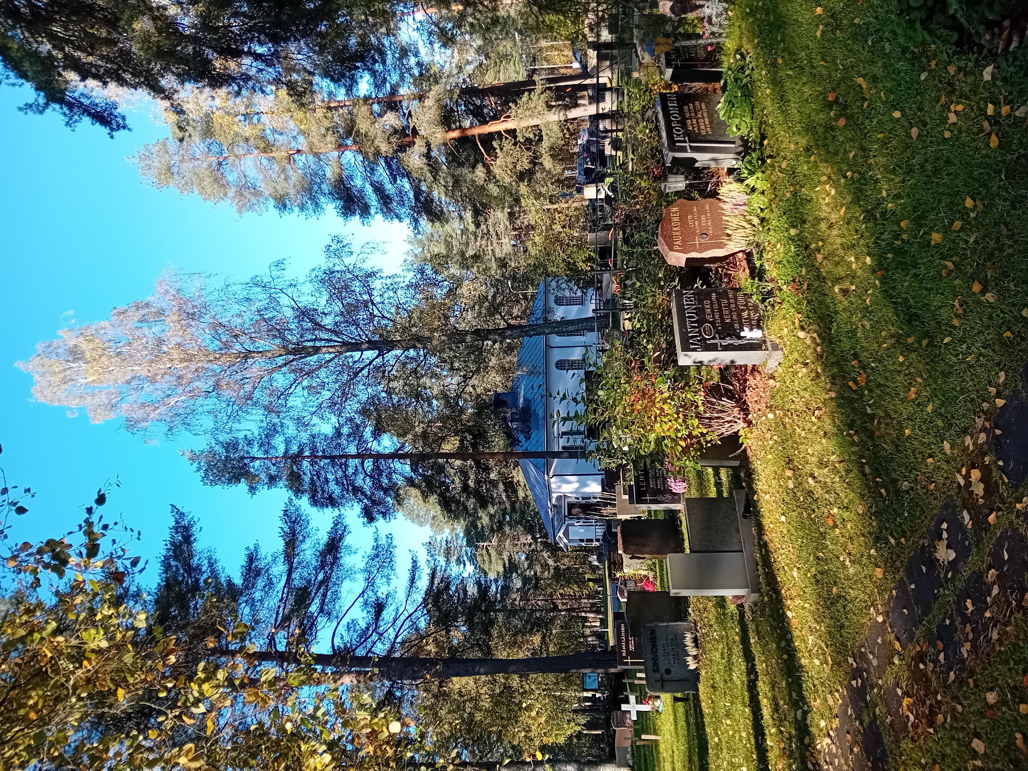 Hautamuistomerkkejä nurmikolla, taustalla näkyy siunauskappeli.
