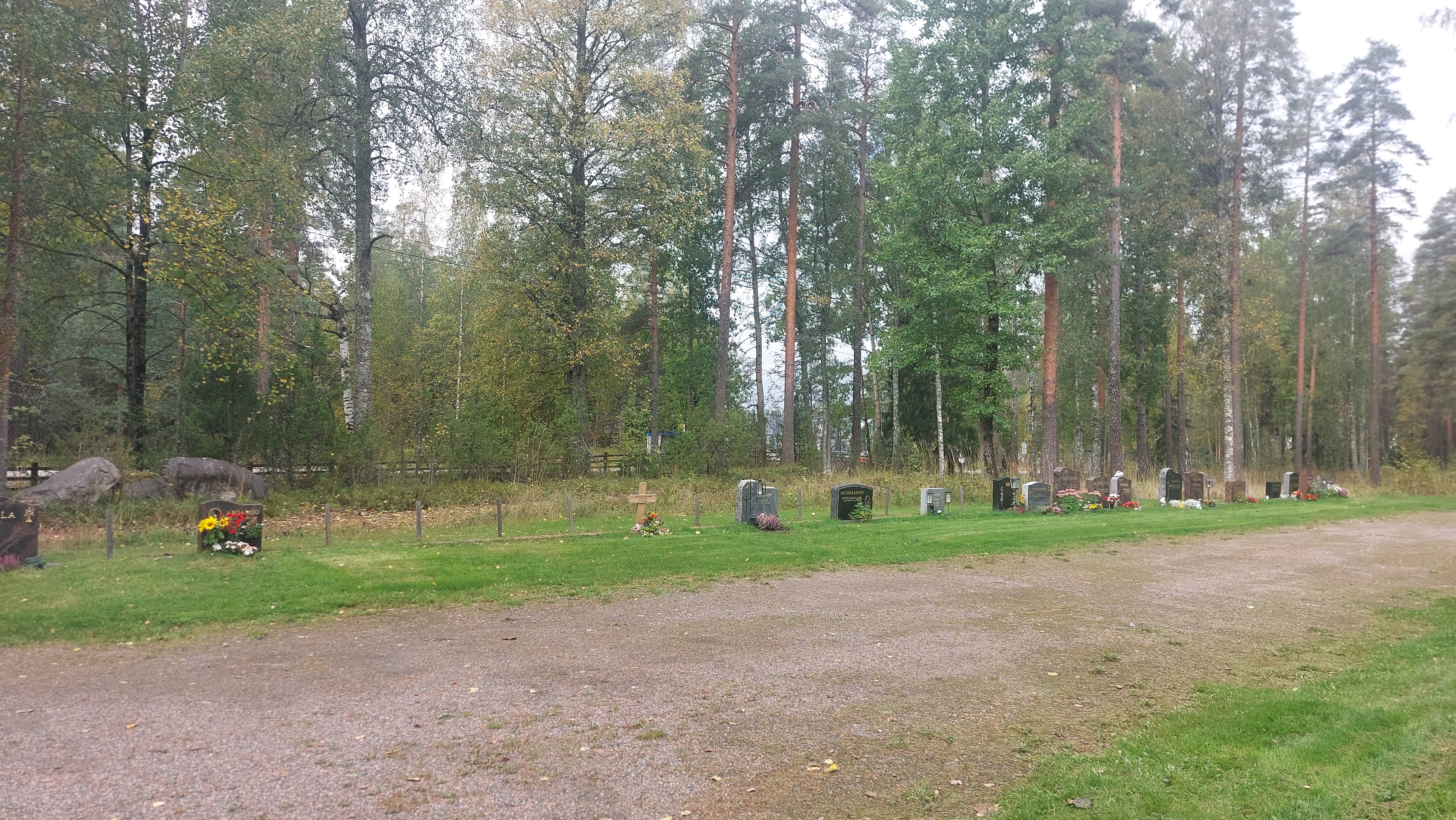 Hautamuistomerkkejä nurmikolla. Edessä hiekkakäytävä, taustalla puita.