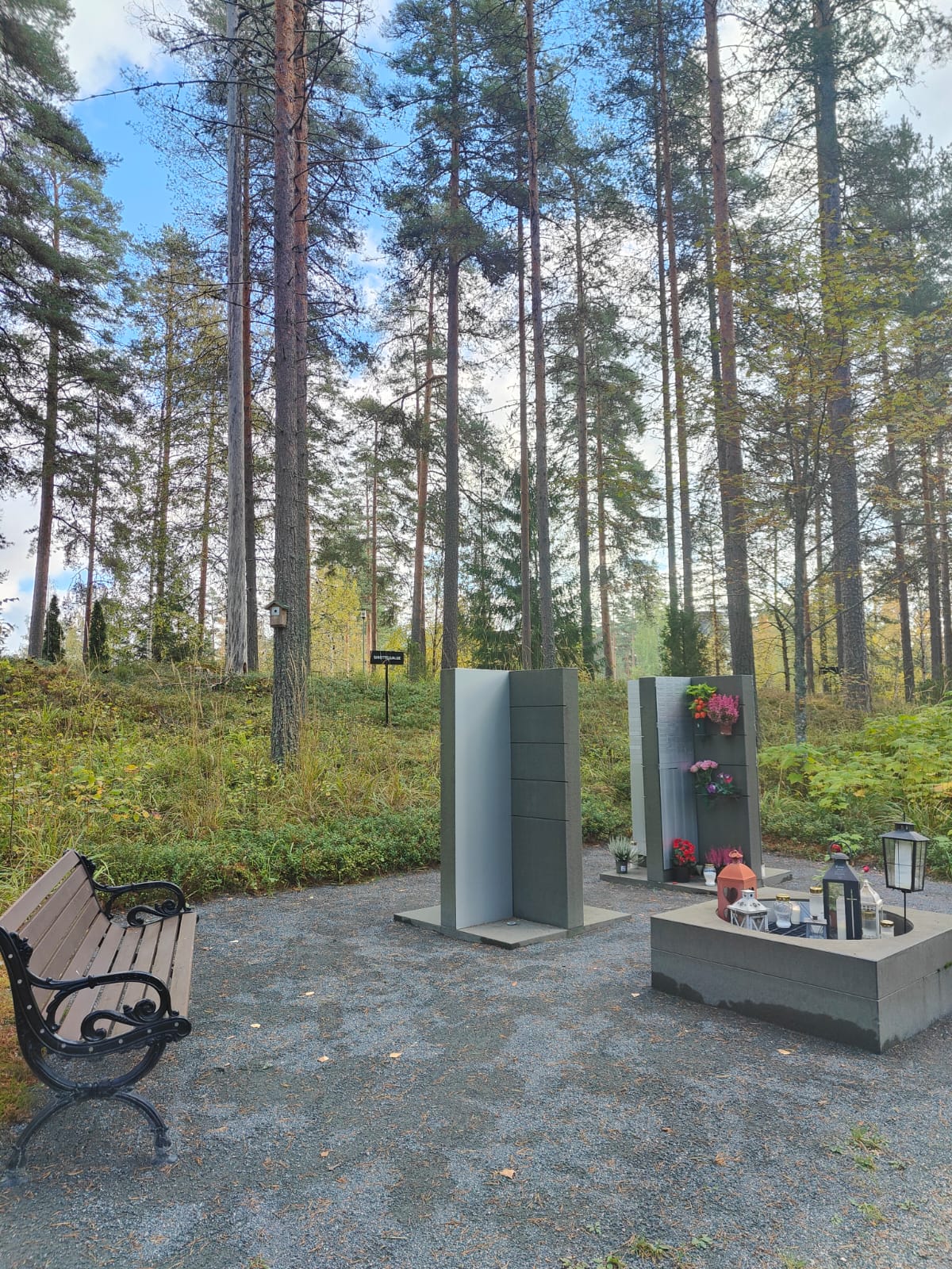 Kaksi yhteishautamuistomerkkiä vainajan nimilaattoja varten. Paikalla myös pieni pöytä kukkia ja kynttilöitä varten.